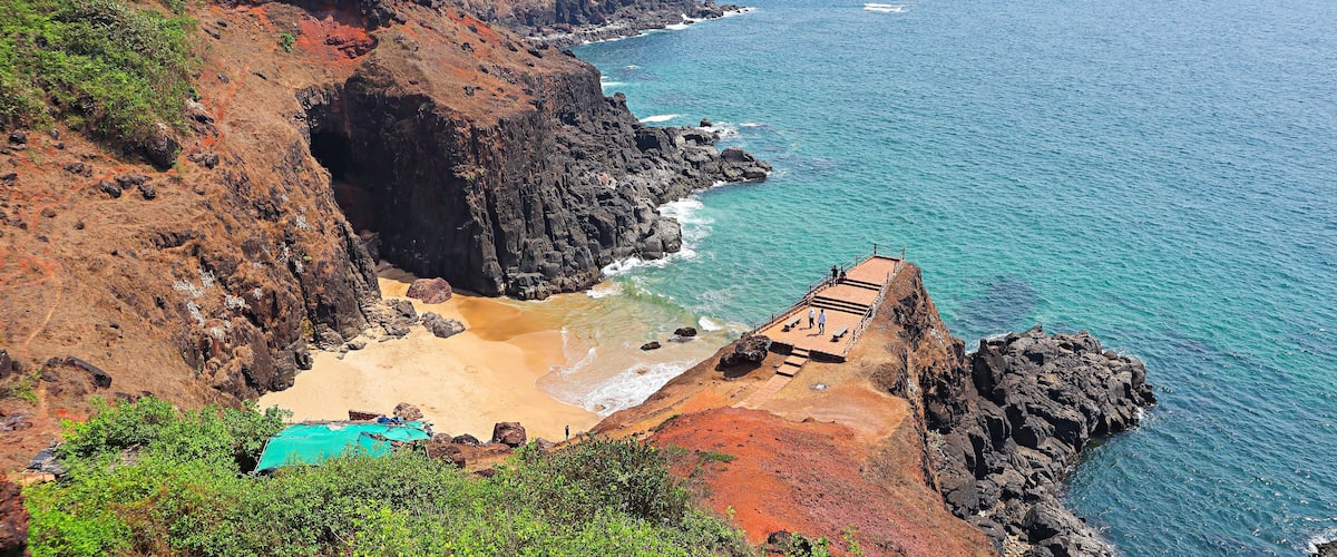 A coastal landscape with a rocky cliff, a beach, and a clear blue sea.