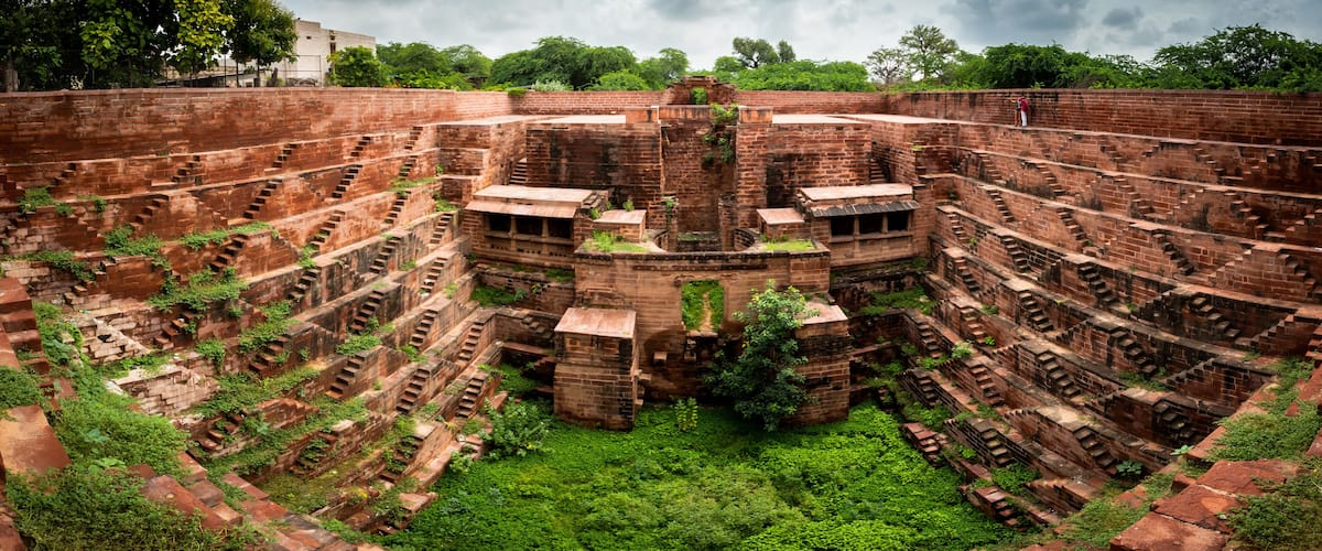 A large, ancient brick amphitheater with multiple tiers of seating, surrounded by lush greenery.