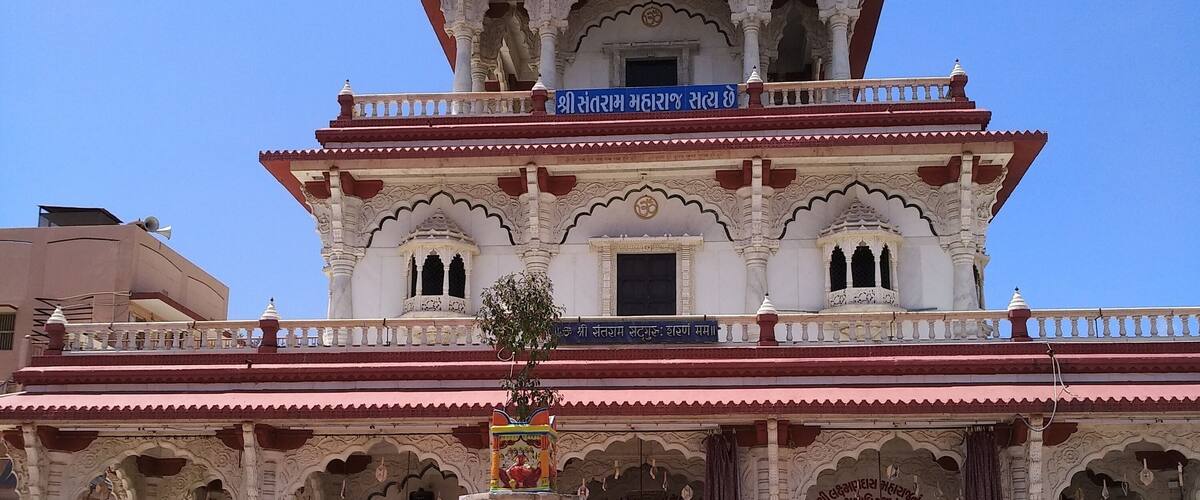 A multi-tiered temple with intricate white and red architecture, a central fountain, and a clear blue sky.