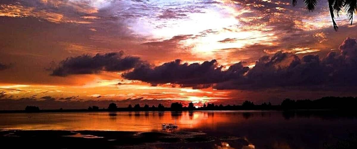 A sunset over a calm lake with reflections of the sky, surrounded by trees and a distant shoreline.