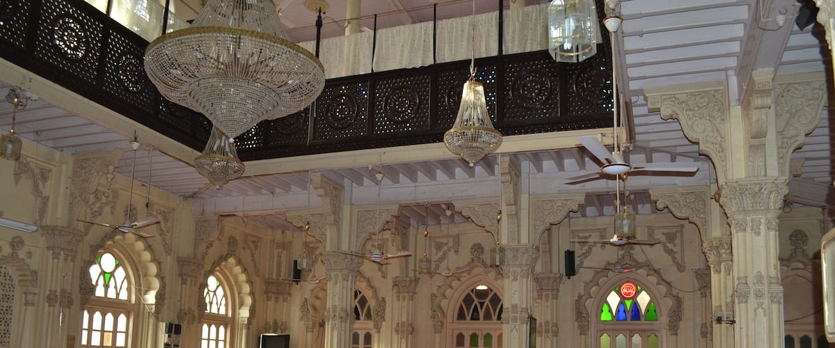 An ornate hall with intricate architectural details, large chandeliers, and stained glass windows.