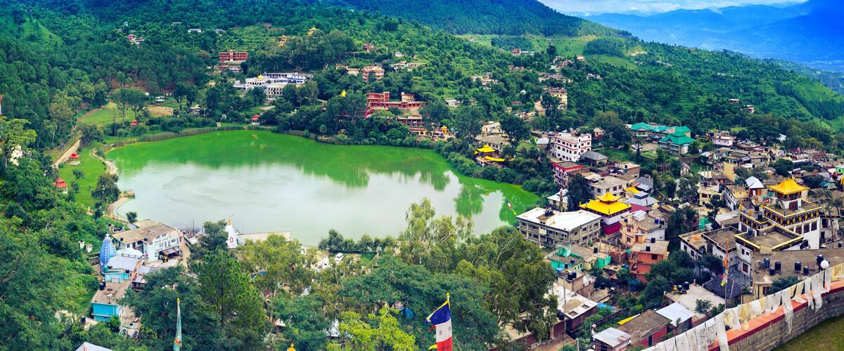 A mountainous village with a central green lake, traditional buildings, and a prominent temple.