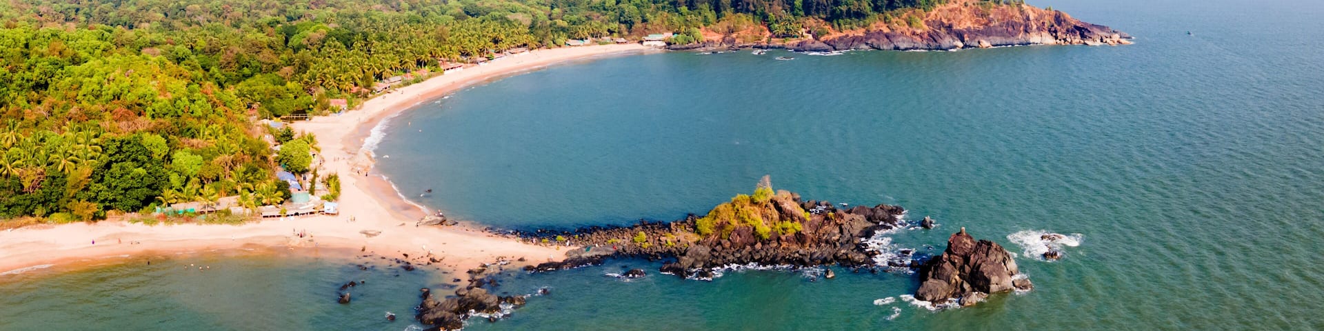 A coastal landscape with a sandy beach, a rocky outcrop, and lush green hills.
