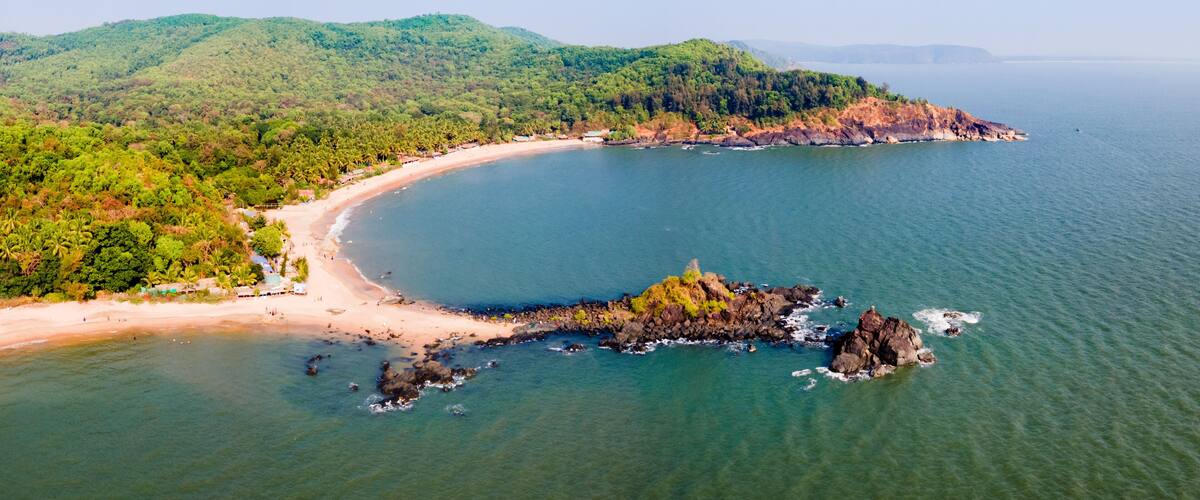 A coastal landscape with a sandy beach, a rocky outcrop, and lush green hills.