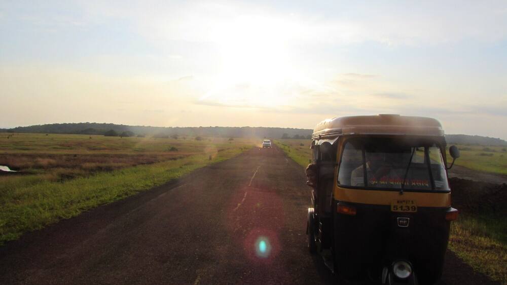 A rural road with a yellow vehicle and a white car.