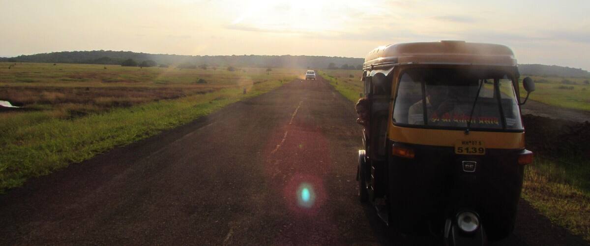 A rural road with a yellow vehicle and a white car.