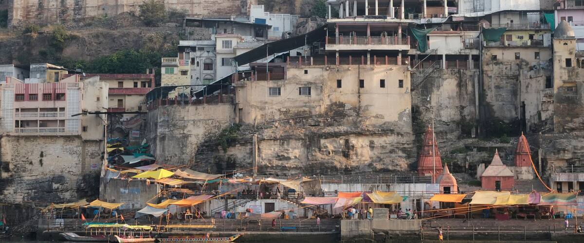 A riverside town with a prominent temple, terraced buildings, and a bustling waterfront with boats and market stalls.