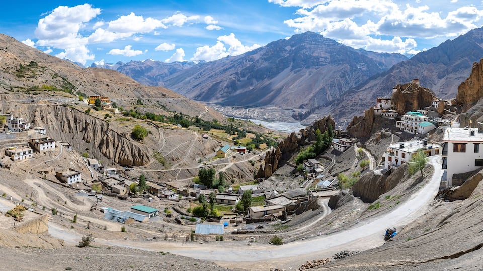 A mountainous village with winding roads, buildings, and a valley with a river.