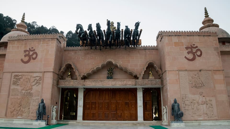 A temple entrance with a large wooden door, statues, and a row of horses on top.