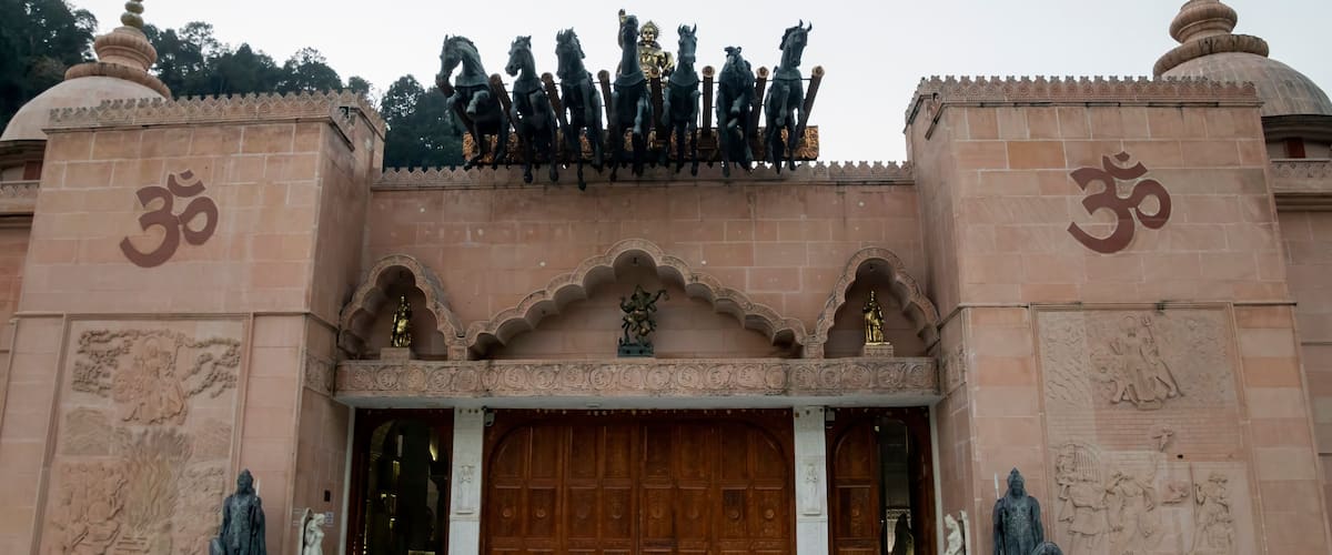 A temple entrance with a large wooden door, statues, and a row of horses on top.