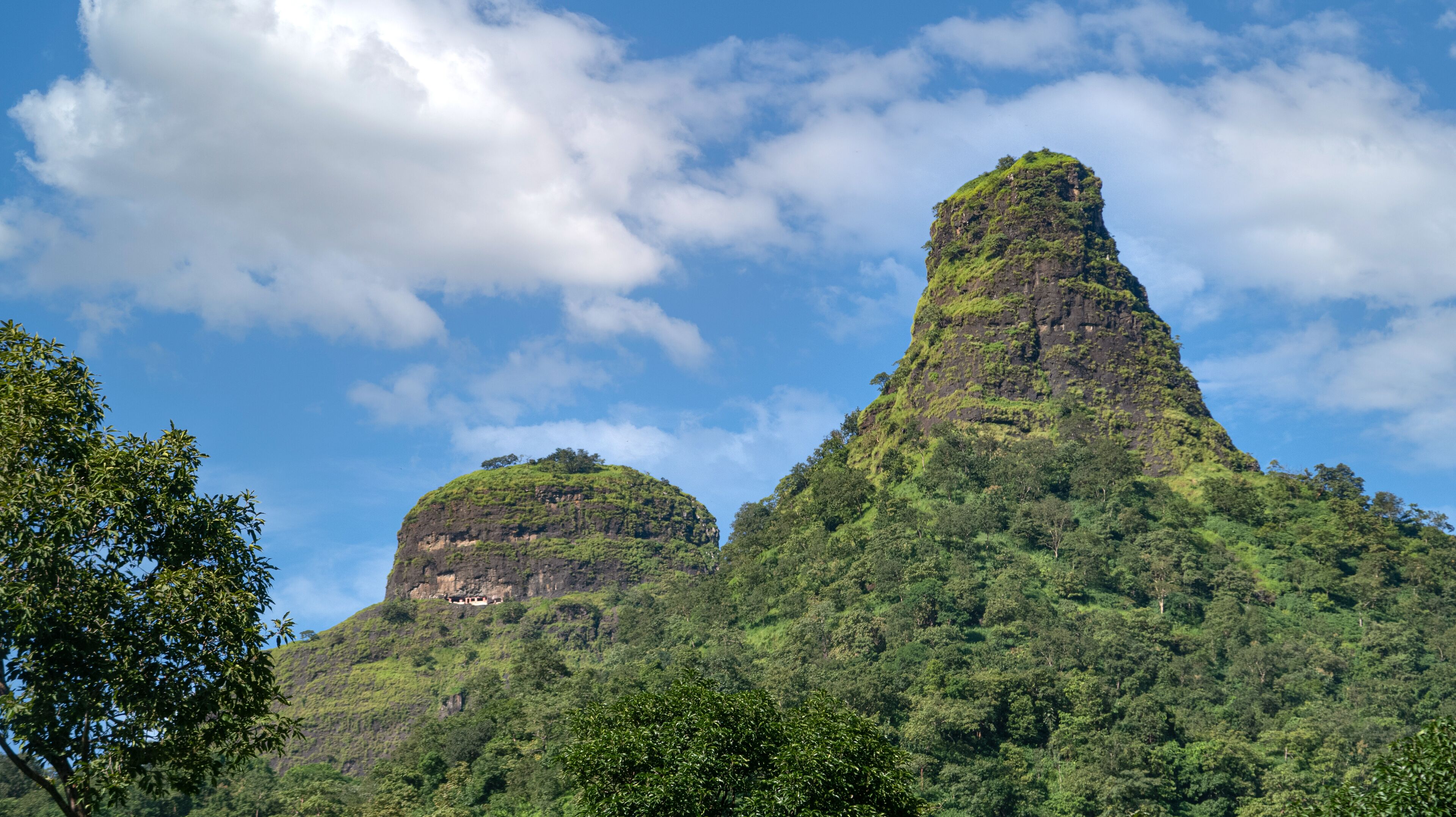 Two prominent mountain peaks with lush green vegetation, set against a partly cloudy sky.