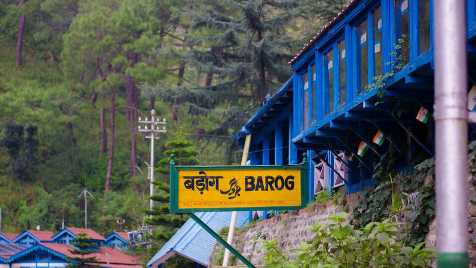 A signboard with text in a non-Latin script, a blue building with a sloped roof, and a mountainous backdrop.