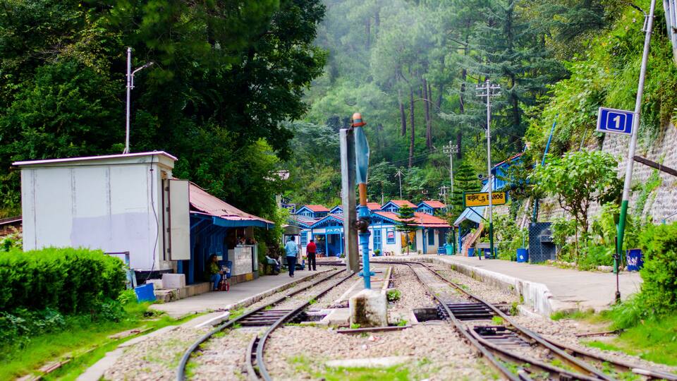 A railway station surrounded by lush greenery and traditional buildings.