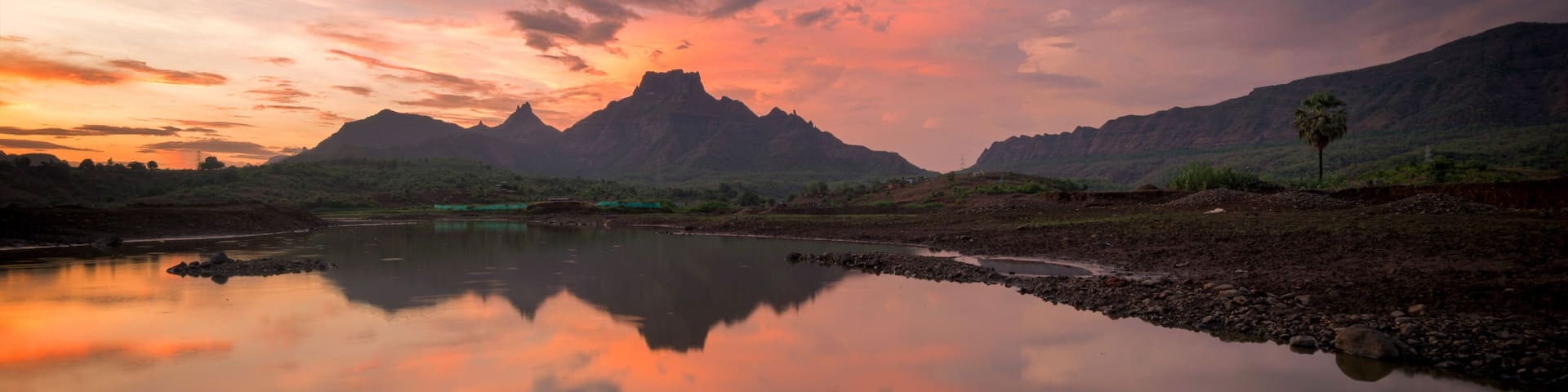 A calm river reflecting the sky, surrounded by mountains and sparse vegetation.