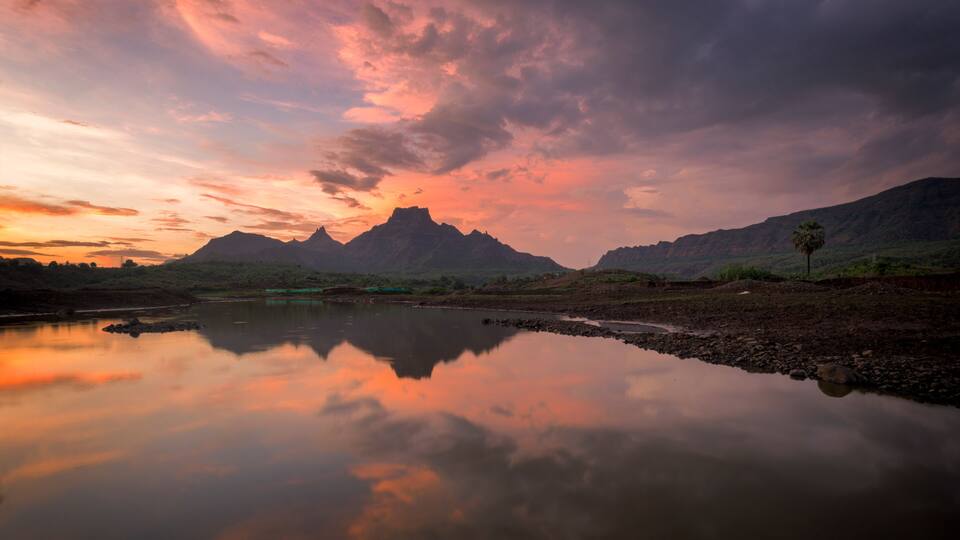 A calm river reflecting the sky, surrounded by mountains and sparse vegetation.
