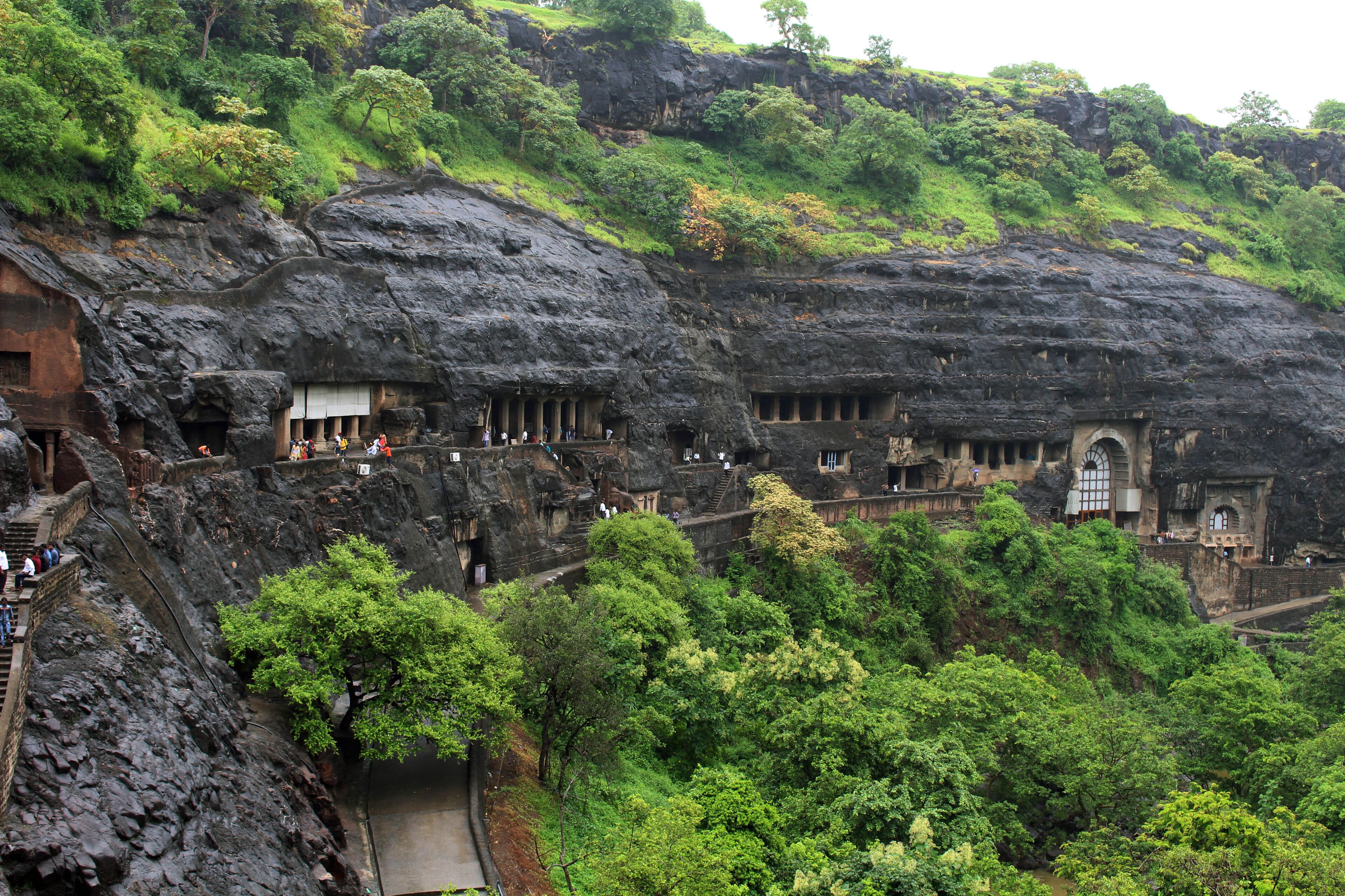 A rock-cut temple complex with multiple structures carved into the cliff face, surrounded by lush greenery.