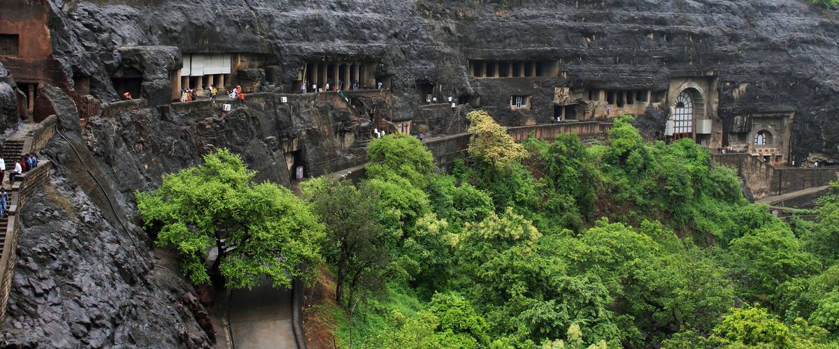 A rock-cut temple complex with multiple structures carved into the cliff face, surrounded by lush greenery.