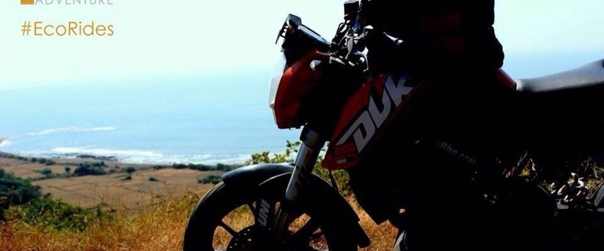 A motorcycle parked on a dirt path with a scenic view of the ocean and hills in the background.