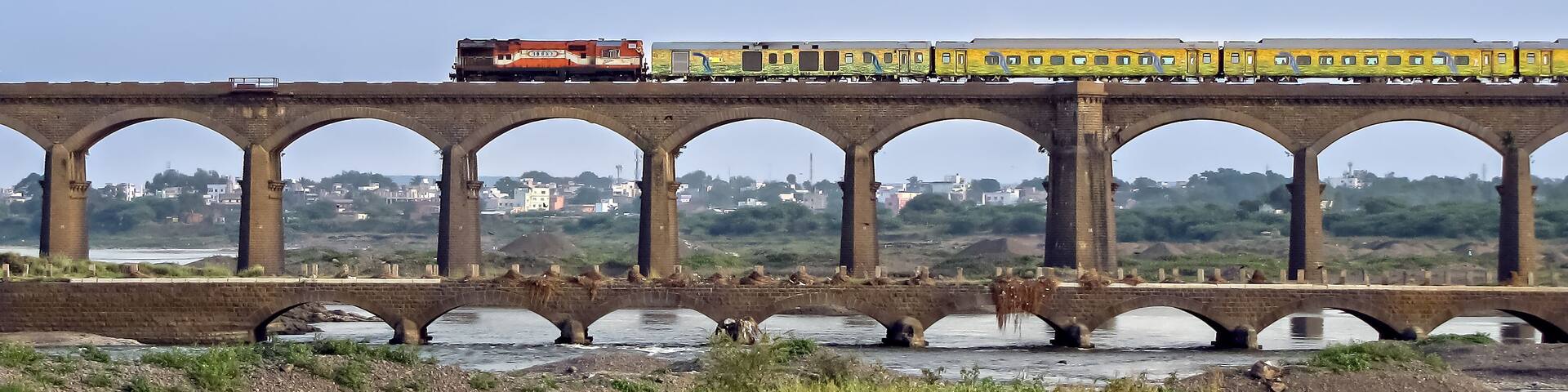 On its inaugural run, super-fast Duronto express train crossing an old stone arc bridge in Daund, Maharashtra, India