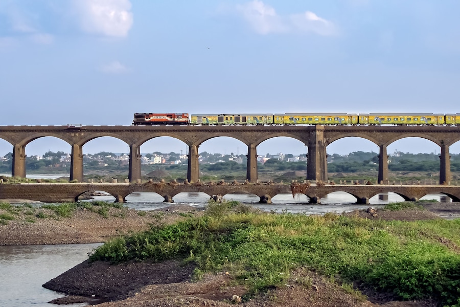 On its inaugural run, super-fast Duronto express train crossing an old stone arc bridge in Daund, Maharashtra, India