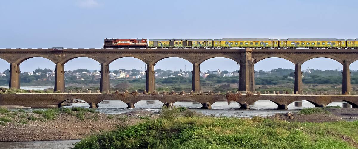 A train crossing a bridge over a river with greenery in the foreground.