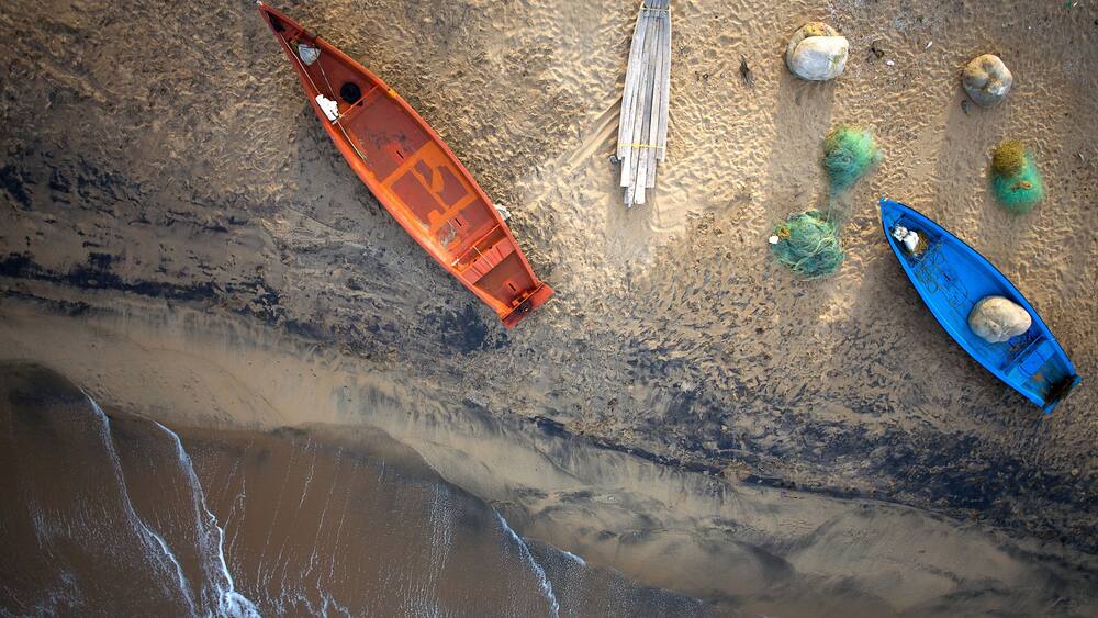 An aerial view of a beach with two boats, a wooden ladder, and some rocks.