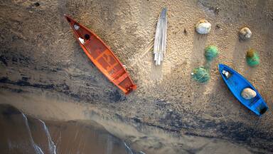 An aerial view of a beach with two boats, a wooden ladder, and some rocks.