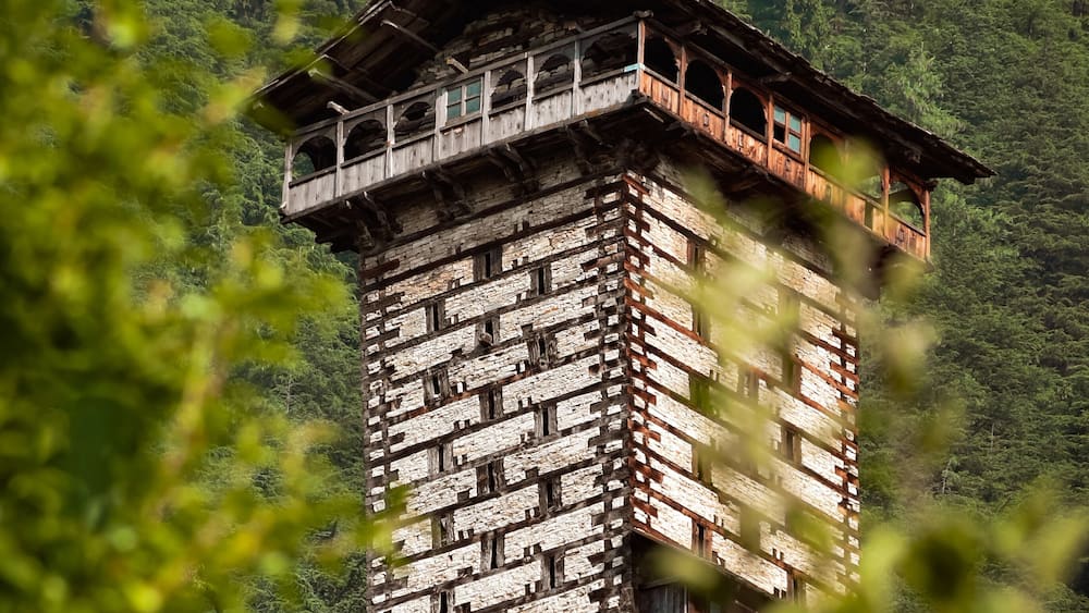 Ein traditioneller Holzturm mit einem Balkon, vor einer üppigen grünen Berglandschaft.