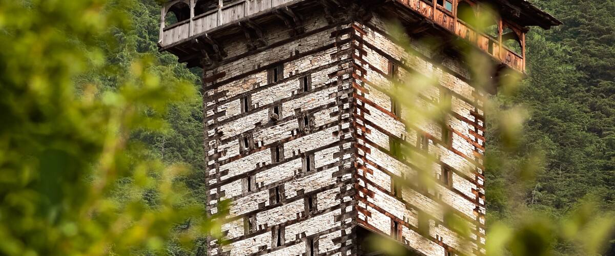 A traditional wooden tower with a balcony, set against a lush green mountain backdrop.