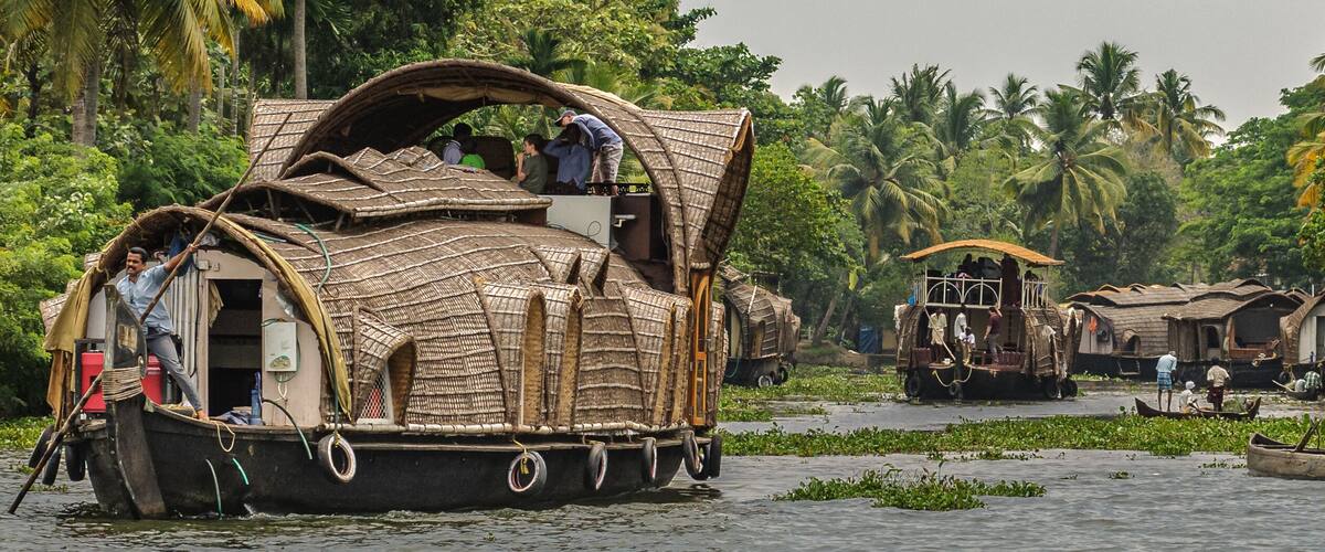 A traditional houseboat on a river surrounded by lush greenery and palm trees.