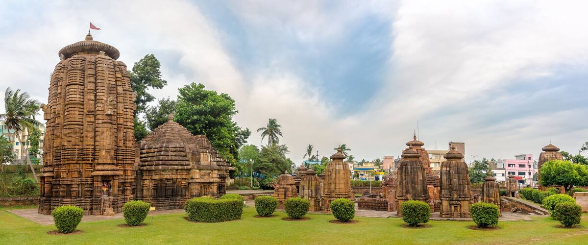 Ancient stone structures with intricate carvings, surrounded by well-maintained greenery and palm trees.