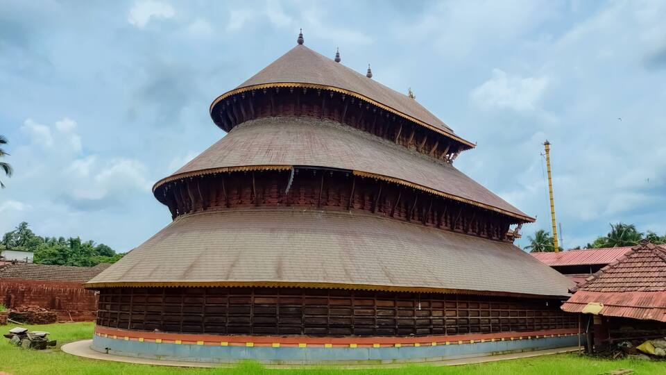 A traditional multi-tiered building with a conical roof, surrounded by green grass and palm trees.