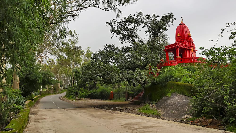 A red temple with a dome, surrounded by lush greenery and a winding road.
