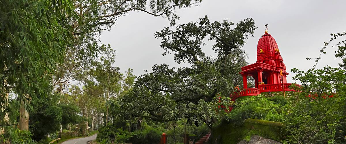 A red temple with a dome, surrounded by lush greenery and a winding road.
