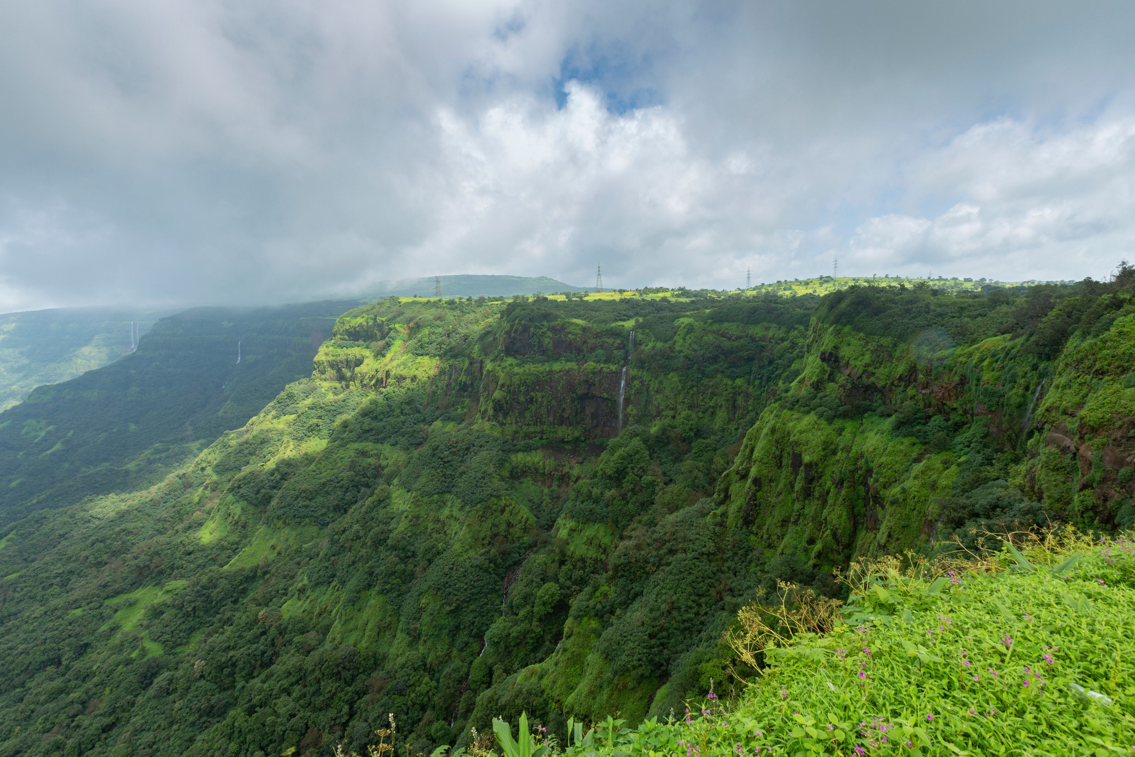 A lush green valley with steep cliffs and a waterfall.