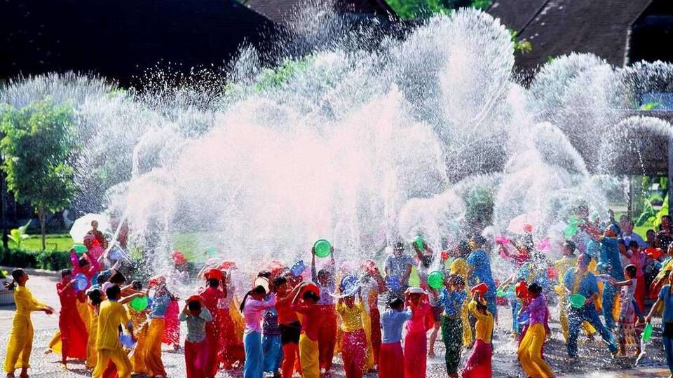 A group of people in colorful costumes dancing in a water fountain.