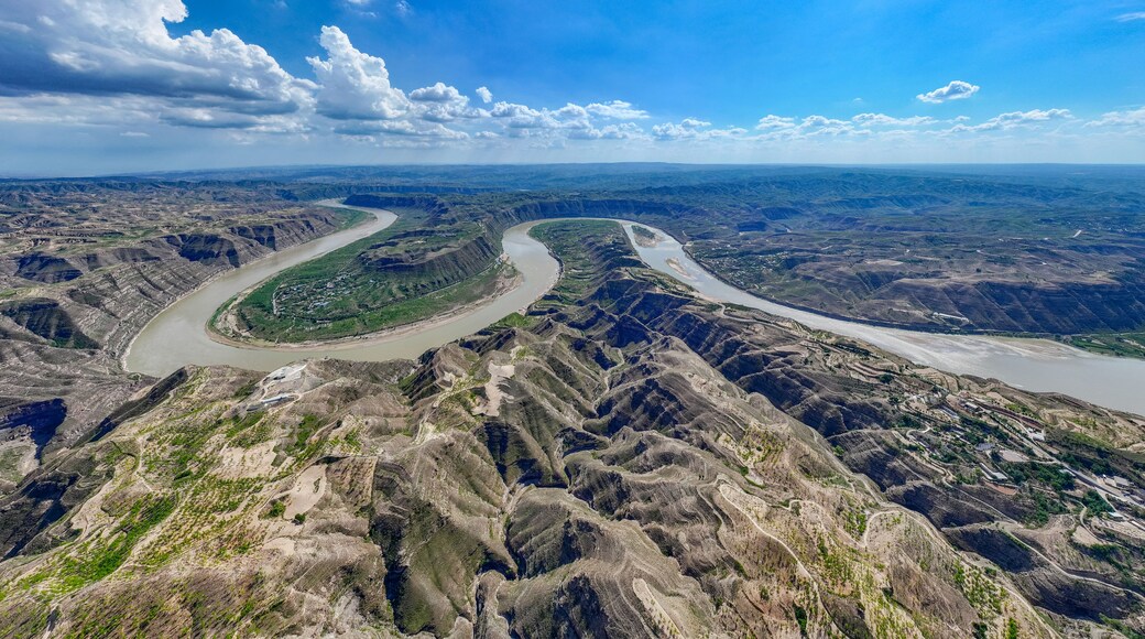 Un río serpentea por un paisaje de cañón accidentado con vegetación escasa y edificios a lo lejos.