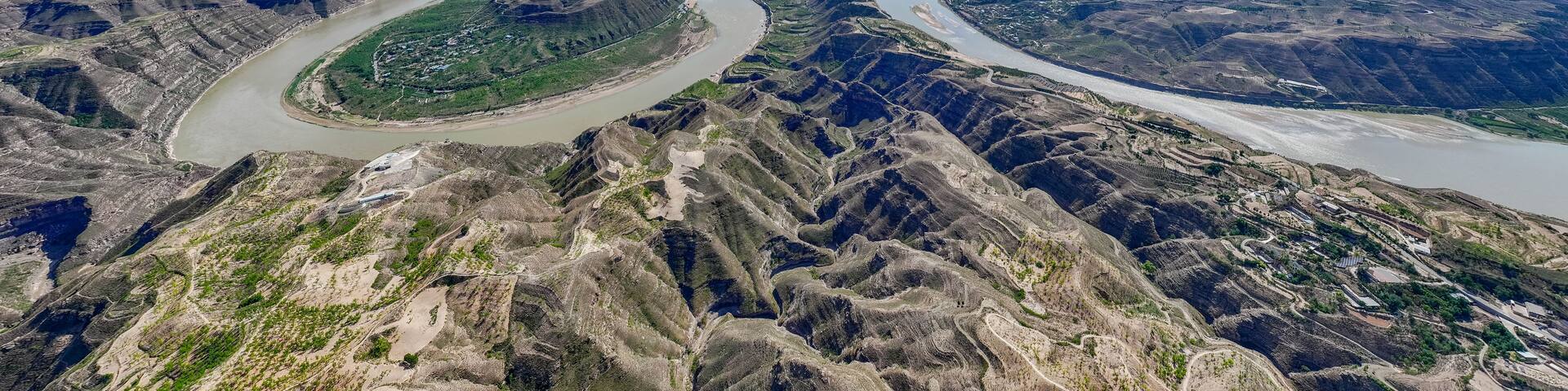 A river winding through a rugged canyon landscape with sparse vegetation and distant buildings.