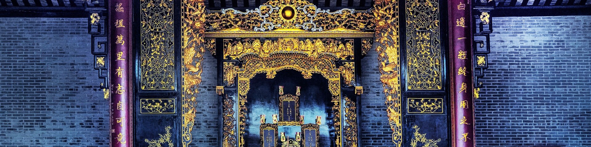 Um templo chinês tradicional com ornamentos dourados elaborados, lanternas vermelhas e um altar central.