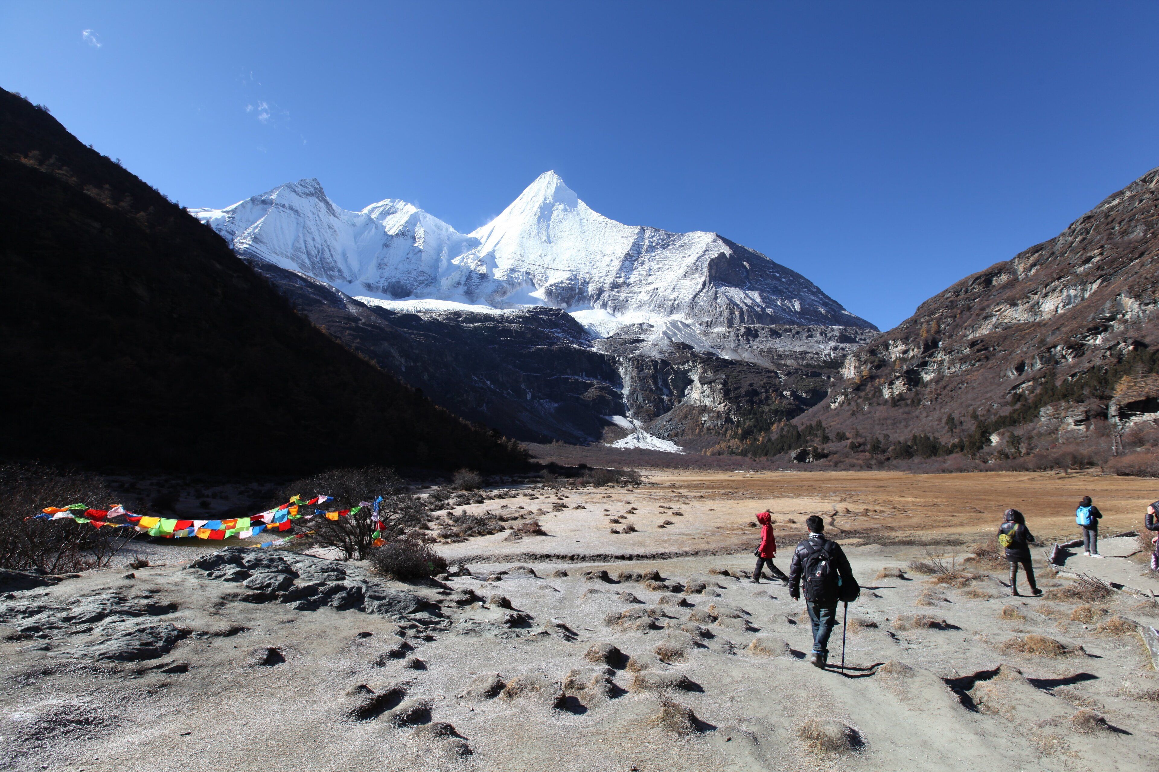 A mountainous landscape with trekkers, a snow-capped peak, and prayer flags.