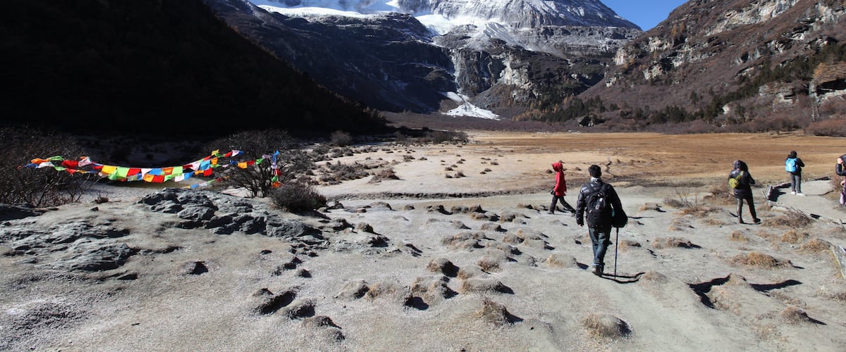 A mountainous landscape with trekkers, a snow-capped peak, and prayer flags.