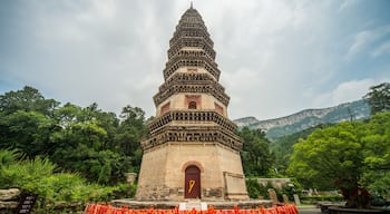 A multi-tiered pagoda with a red door, surrounded by lush greenery and mountains in the background.