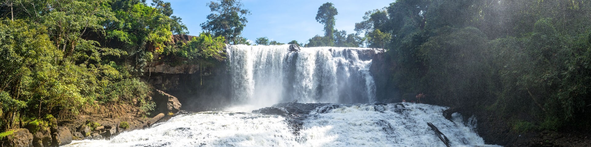 A waterfall cascading over a rocky cliff into a river surrounded by dense forest.