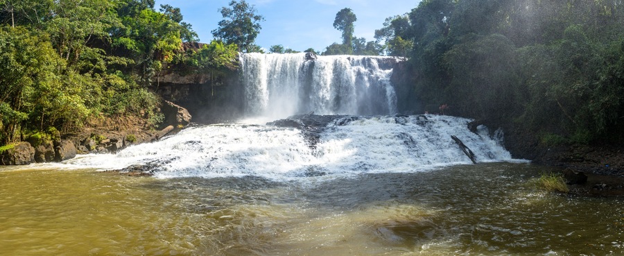 A waterfall cascading over a rocky cliff into a river surrounded by dense forest.