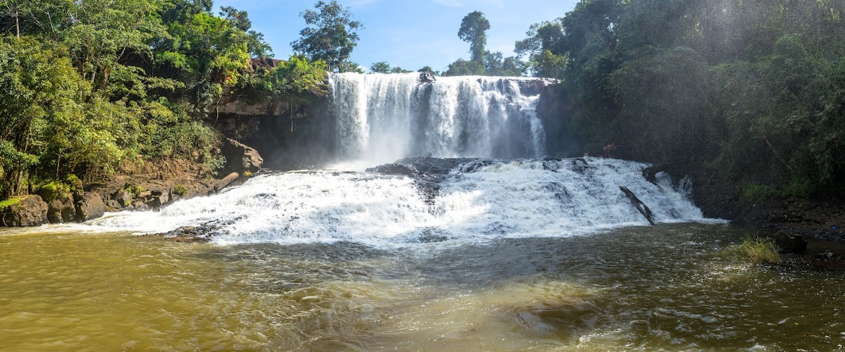 A waterfall cascading over a rocky cliff into a river surrounded by dense forest.