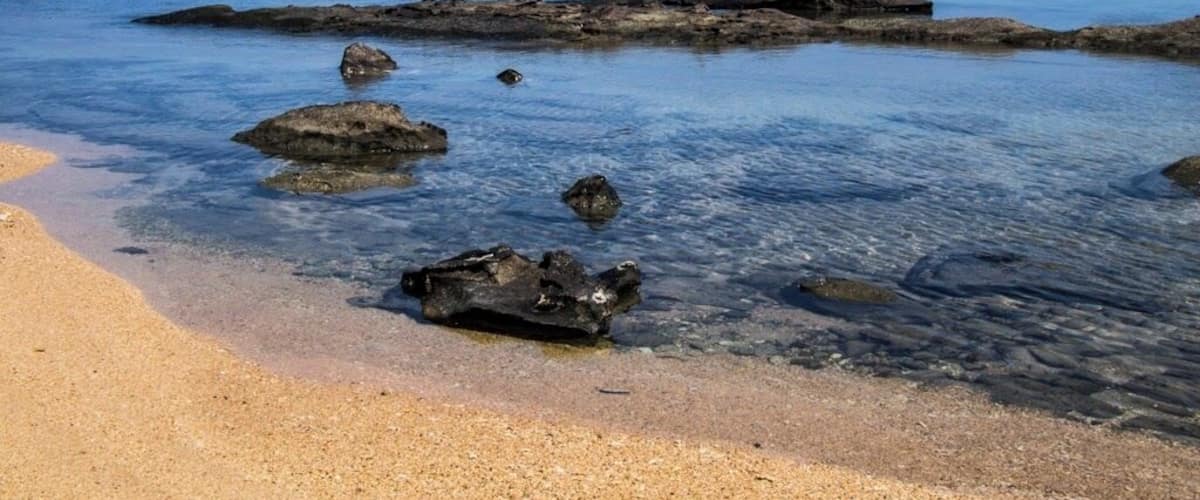A beach with clear water, rocks, and distant islands.