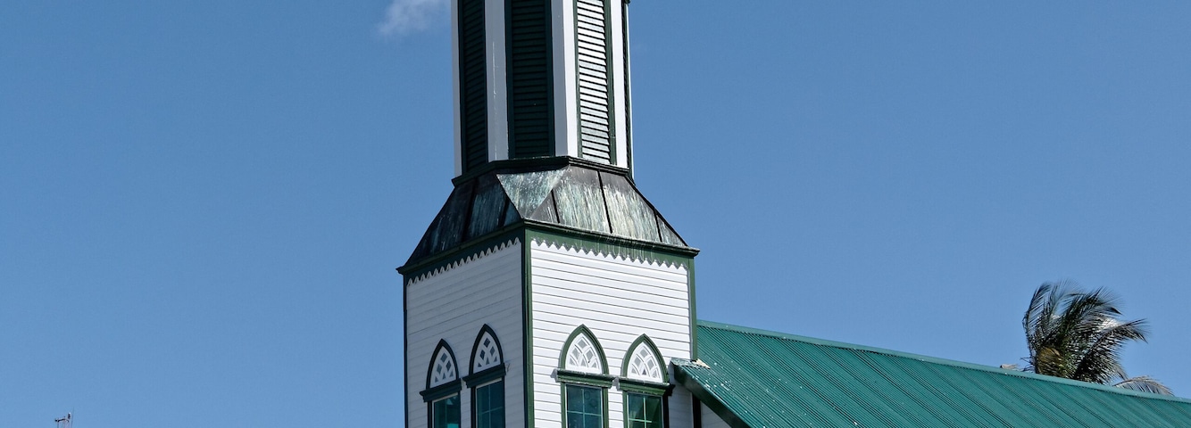 Una iglesia con un campanario alto y ventanas verdes.