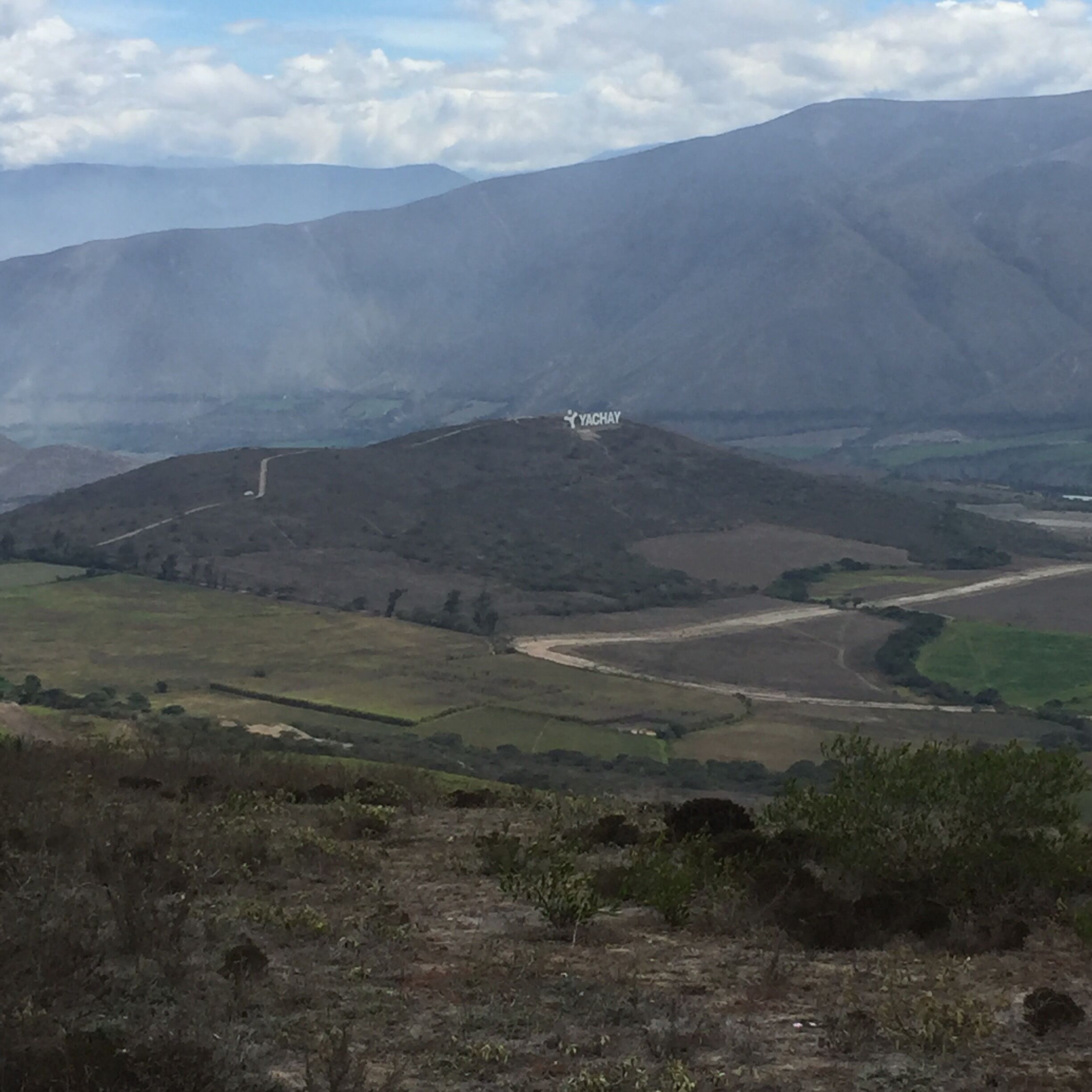A mountainous landscape with a winding road and a small building labeled 'YACHAY' on a hill.