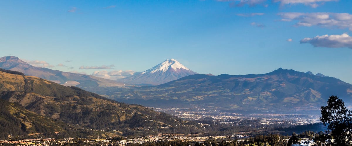 Una cordillera con un pico destacado, un valle con un pueblo y un cielo despejado.