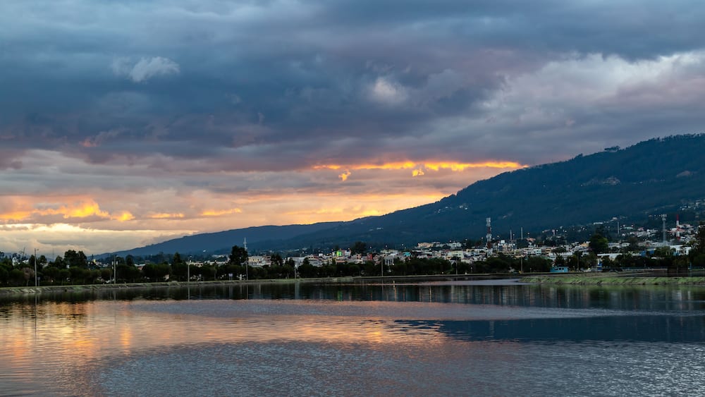 A lake with a city in the background, a cloudy sky, and a sunset.